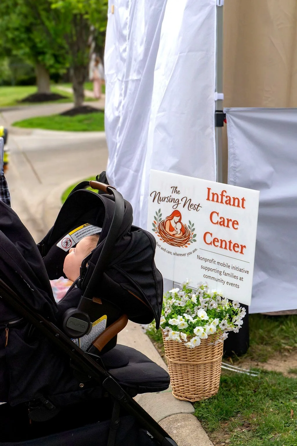 Baby in stroller to the left. The Nursing Nest sign to the right stating Infant Care Center with a basket holding flowers below.