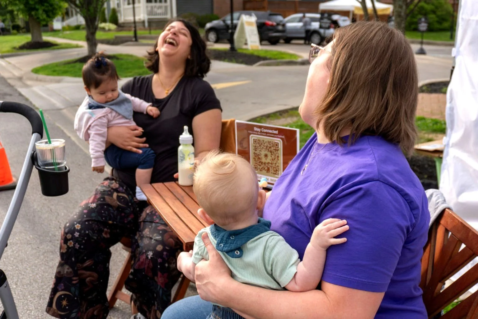 Two women holding babies sitting in chairs laughing