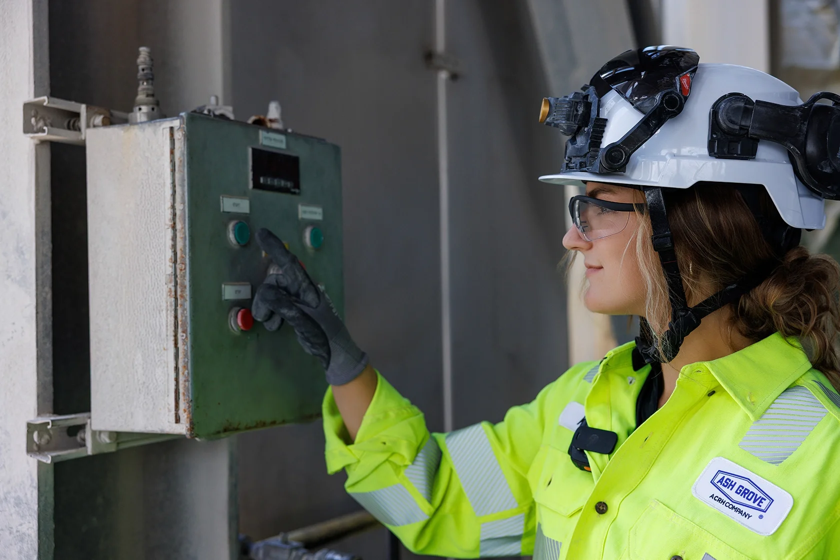 Female worker in safety gear reaching to push a button on a panel
