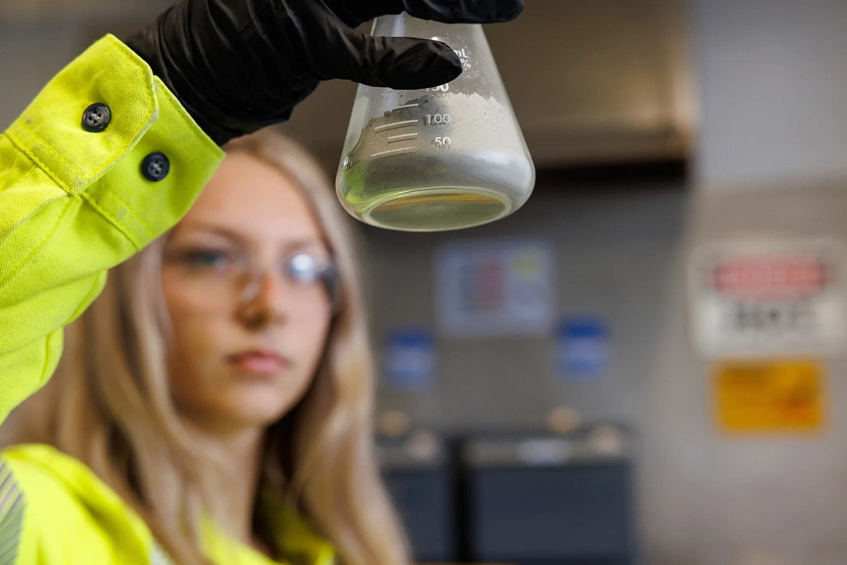 image of a female chemist in safety gear inspecting a beaker with product in it