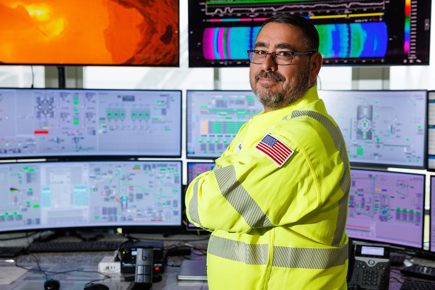 Image of a man in safety gear working in a room of computer monitors that have cement plant data on them