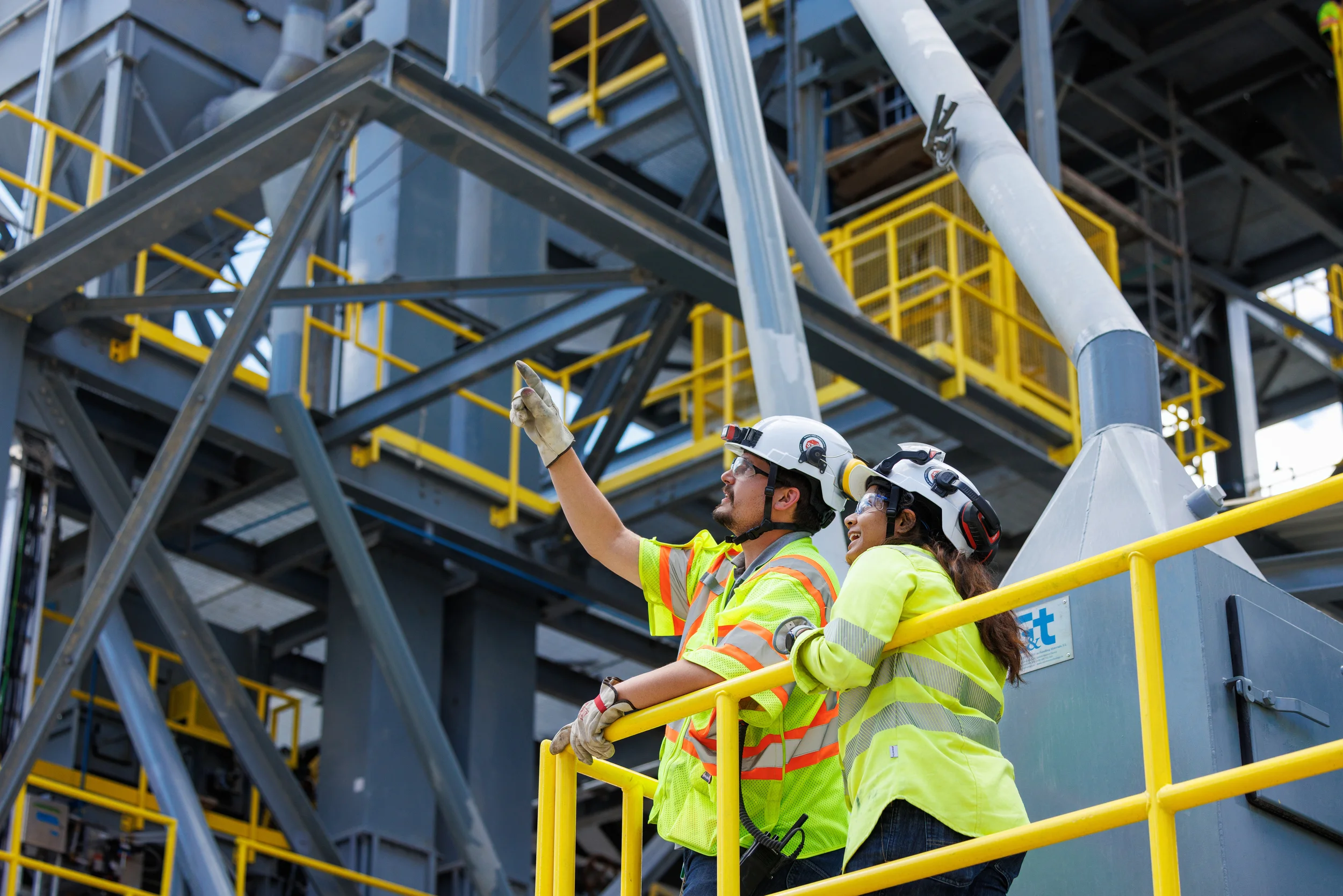 Male and Female workers next to a railing, looking at something above them and pointing at it for discussion