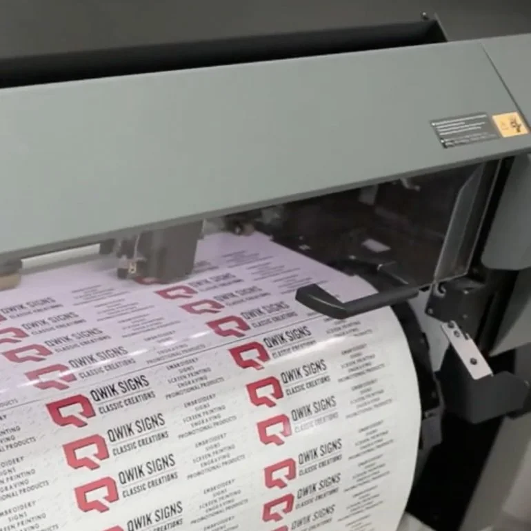 Printer printing sheets with a red logo and text for QWIK SIGNS and classic creations.