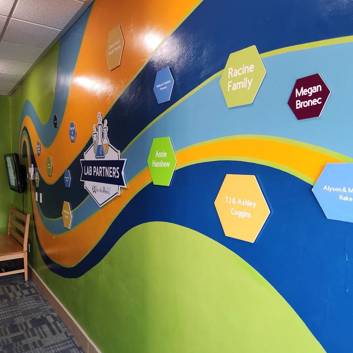 Colorful wall custom mural for Exploration Works in Helena, MT with a winding design, featuring names inside hexagons and a central sign that reads 'Lab Partners' with chemistry icons.