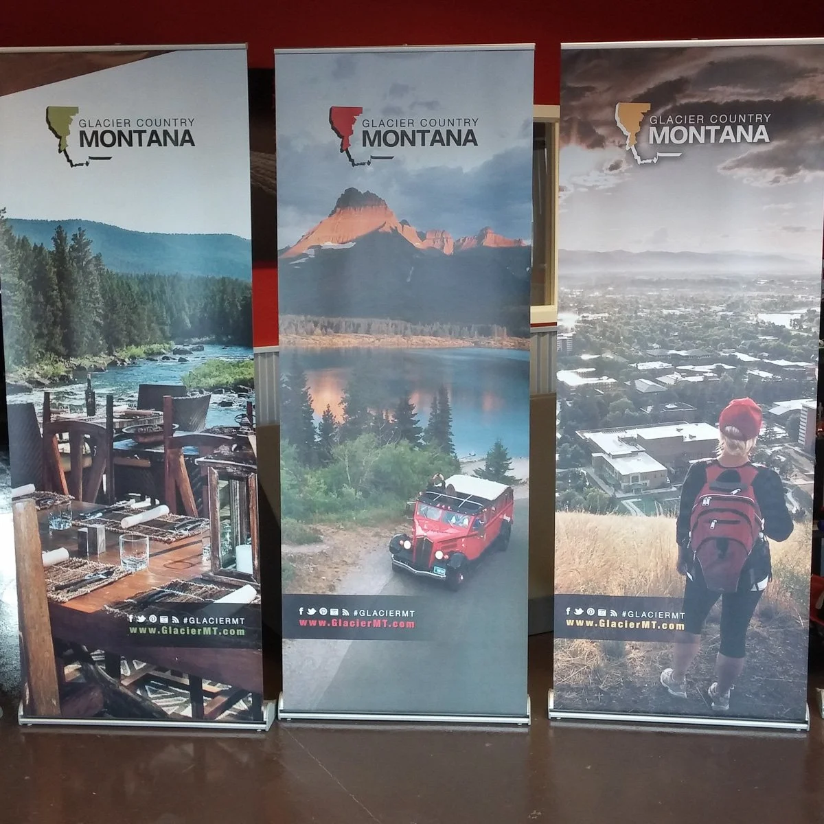 Three custom banners showcasing Glacier County, Montana scenic landscapes: a riverfront dining scene, a mountain with a lake, and a person hiking overlooking a city view.