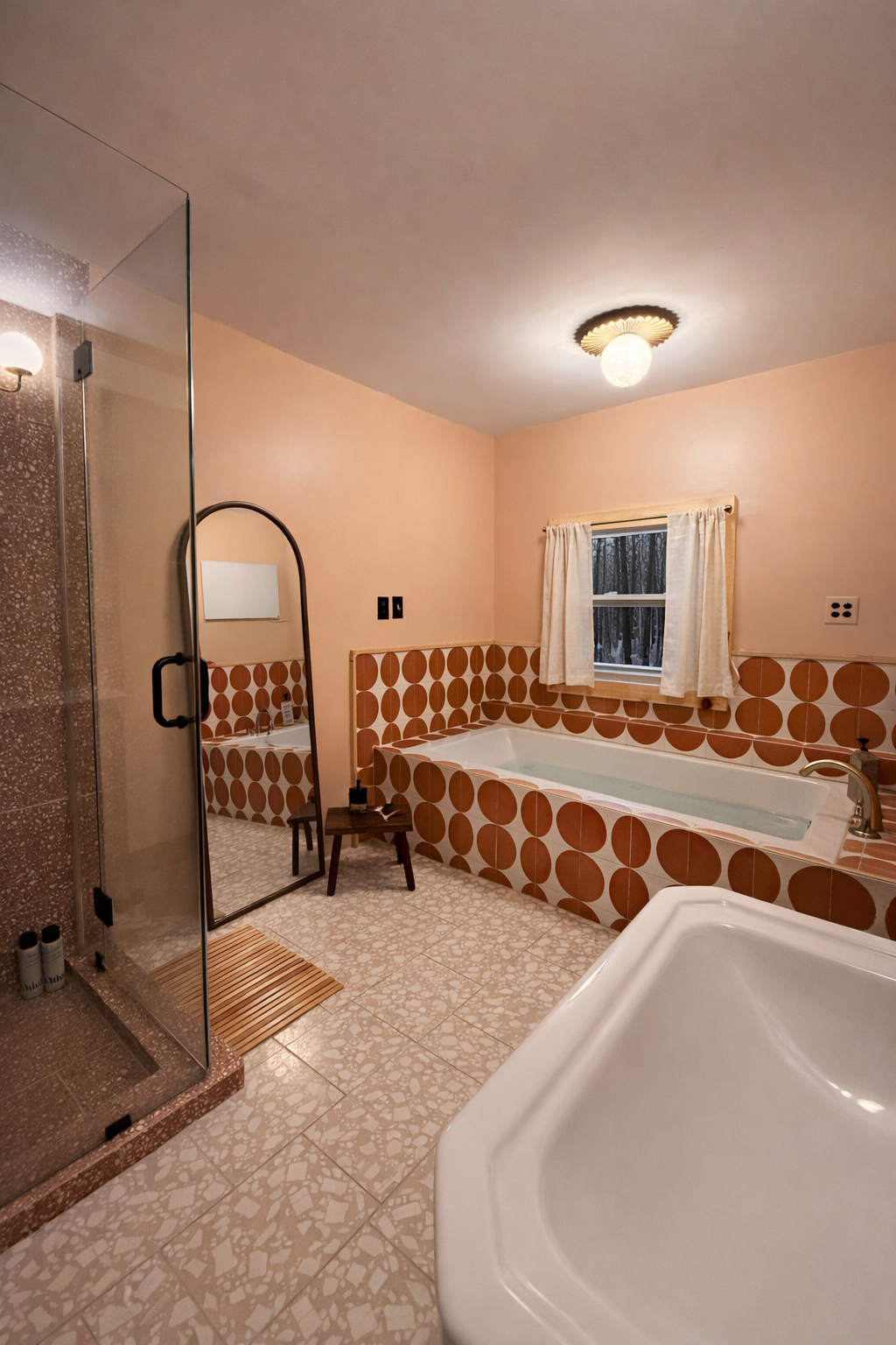 A vintage-style bathroom with a corner shower, a bathtub with brown and white geometric tile design, a small mirror, and a window with curtains, lit by a ceiling light.