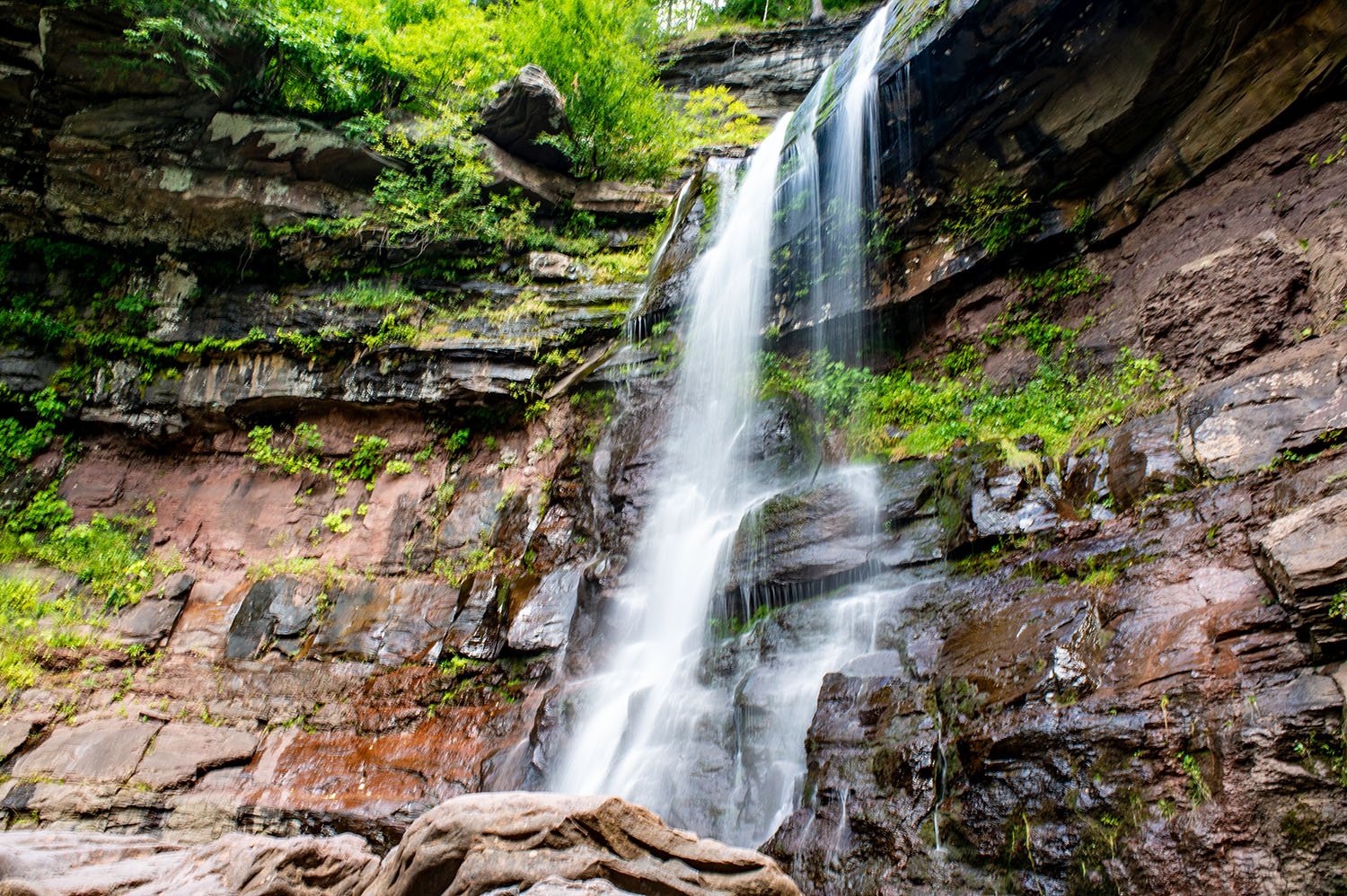A waterfall flowing down a rocky cliff surrounded by green foliage.