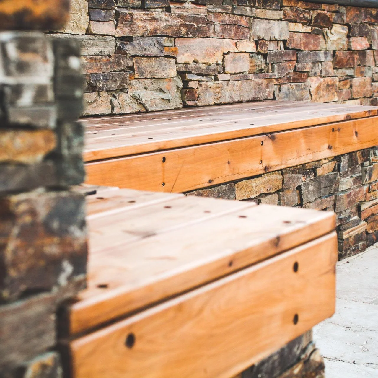 Close-up of wooden and stone seating area with a stone wall in the background.