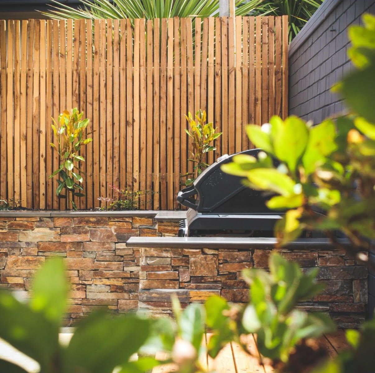 Outdoor area with a wooden privacy fence, potted plants, and a black gas grill on a stone patio.