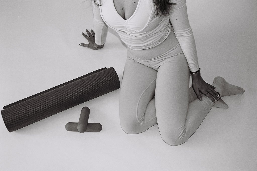 Woman in leggings sitting with mat and hand weights