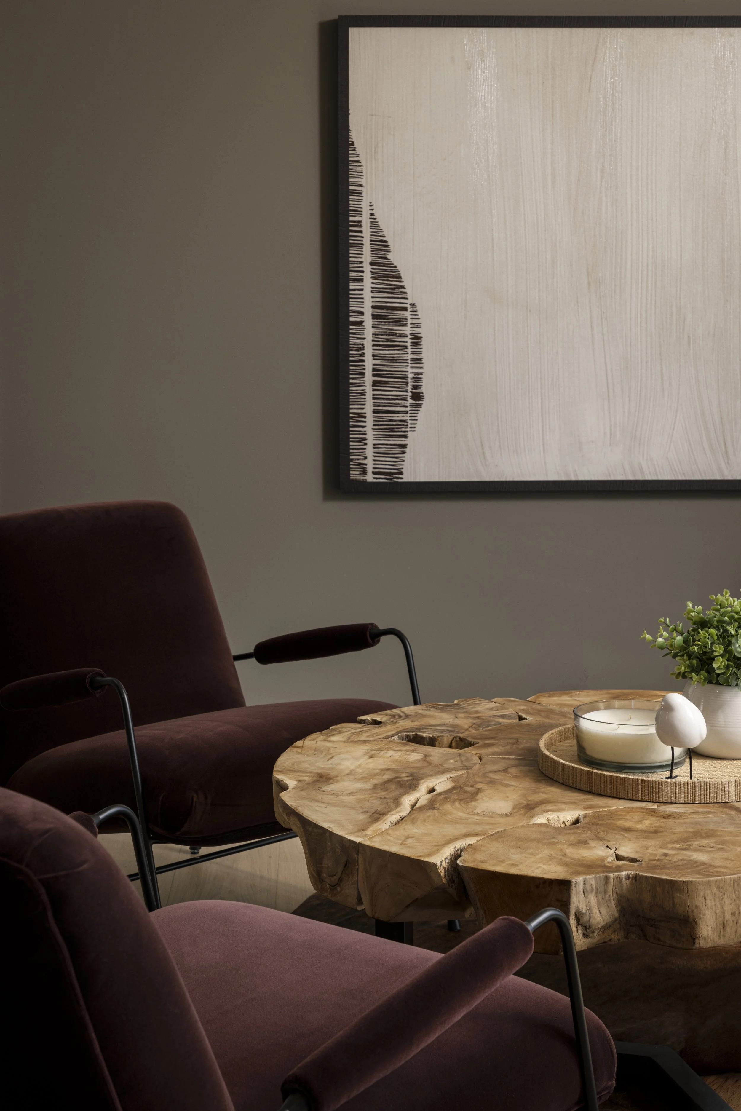 Living room with a dark wood framed abstract painting, velvet armchair, and a rustic wood coffee table with candles and small potted plant.