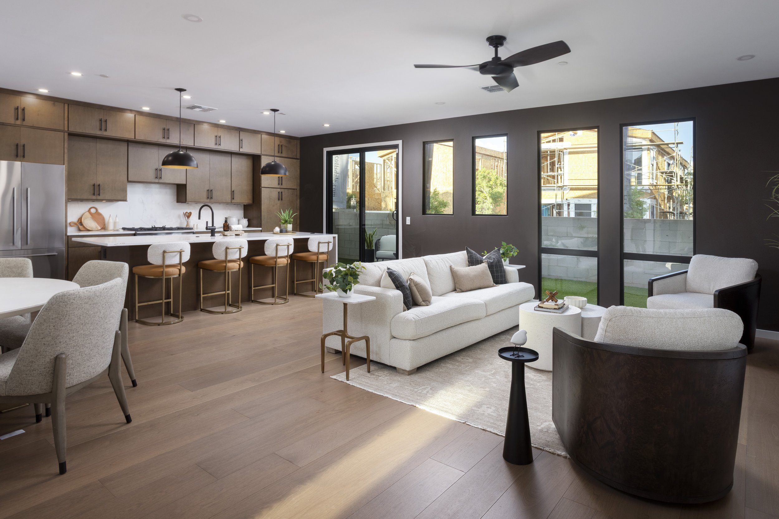 Open-concept living room and kitchen with large windows, white sofa, dining chairs, and hardwood flooring.