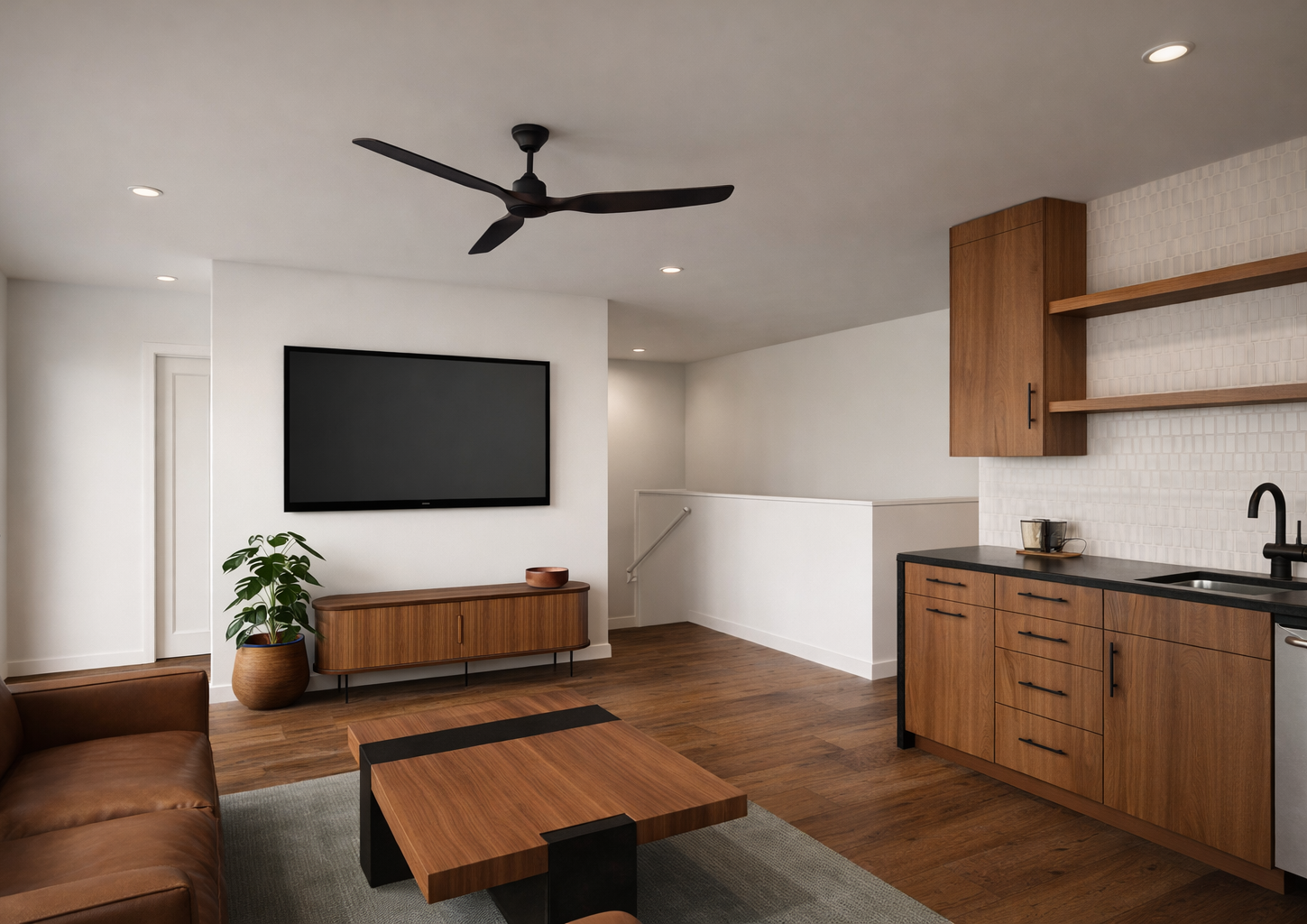 Modern living room with white walls, hardwood floors, a black ceiling fan, a flat-screen TV mounted on the wall, a brown leather sofa, a wooden coffee table, a potted plant, a wooden sideboard, and a kitchen area with wooden cabinets and open shelves
