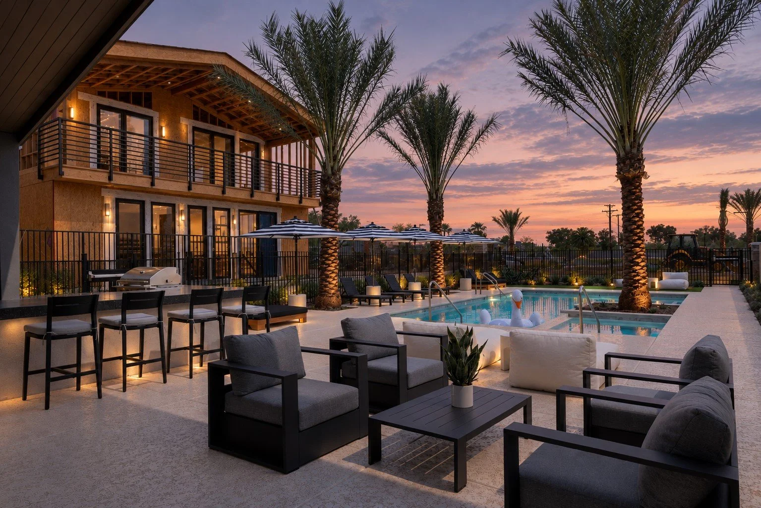 Luxury New Home community with a pool area at sunset, featuring palm trees, lounge chairs, umbrellas, a hot tub, and outdoor seating.