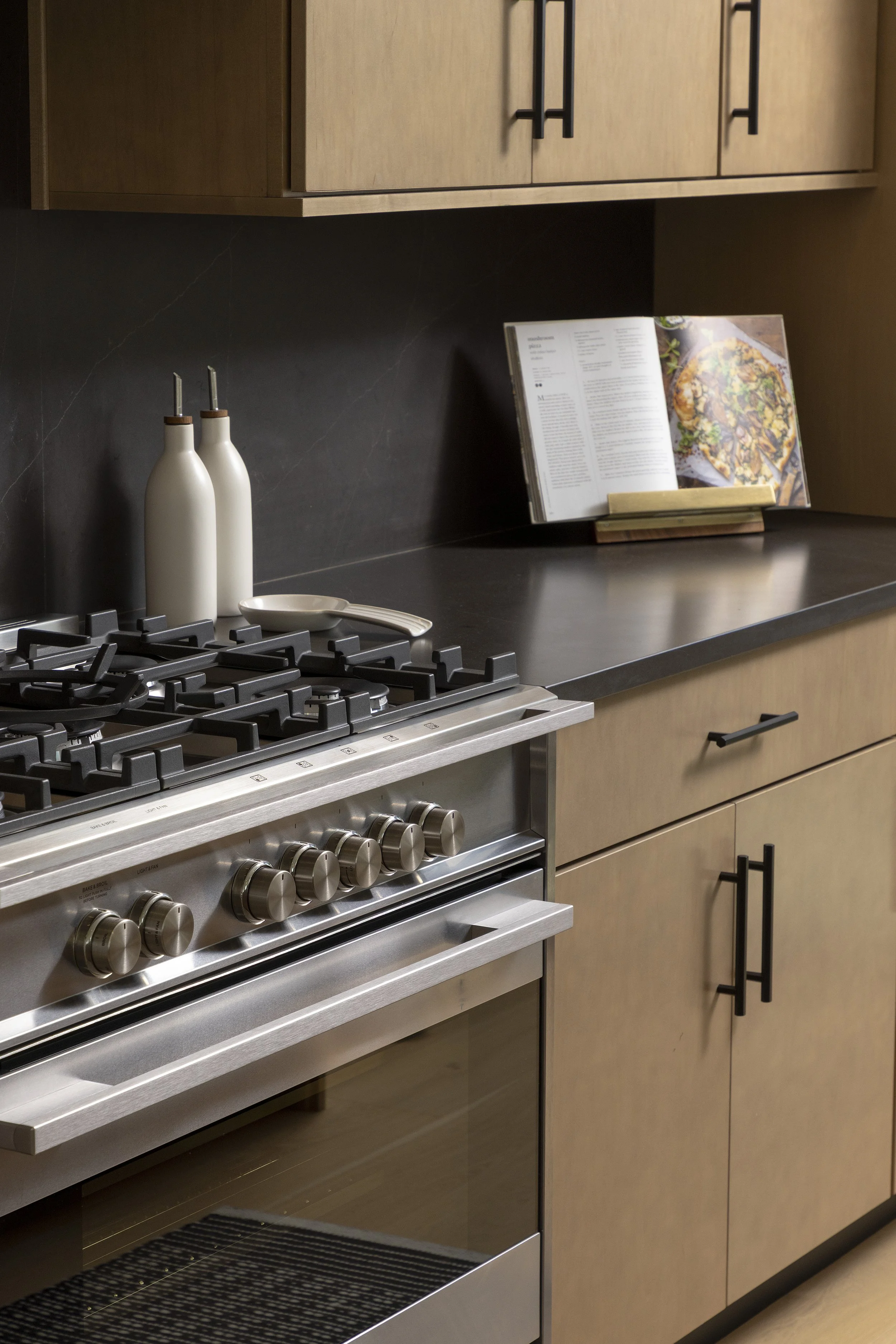 Modern kitchen with stainless steel stove, black countertop, upgraded cabinets, and a full height quartz backsplash with under-cabinet lighting.