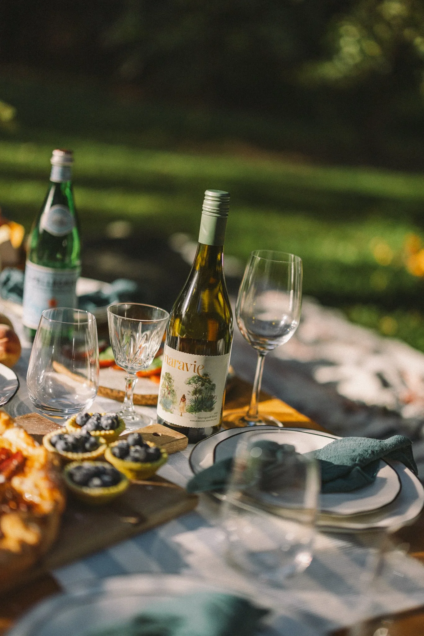 Picnic aesthetic of a table set for outdoor dining with a bottle of white wine, glasses, and various appetizer. Wine pairing ideas and party atmosphere.