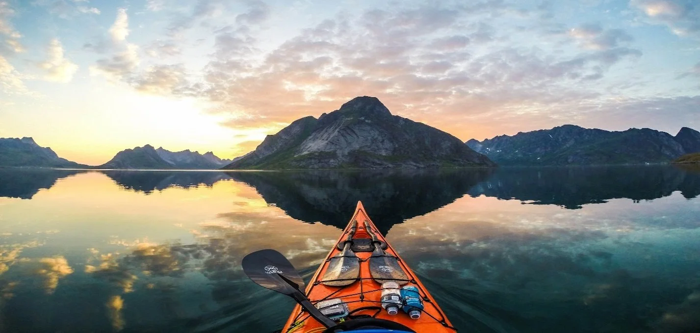 A kayak in calm water with a mountain range and sunset sky reflected on the water's surface.