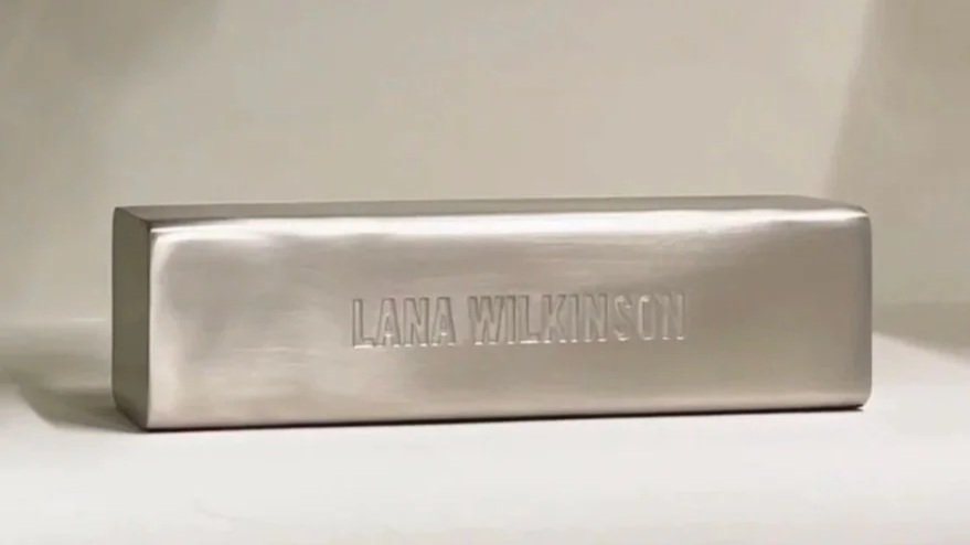 A rectangular metallic object with the name "LANA WILKINSON" engraved on it, placed on a white surface.