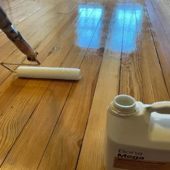 Close-up of a paint roller applying a finish to a hardwood floor.