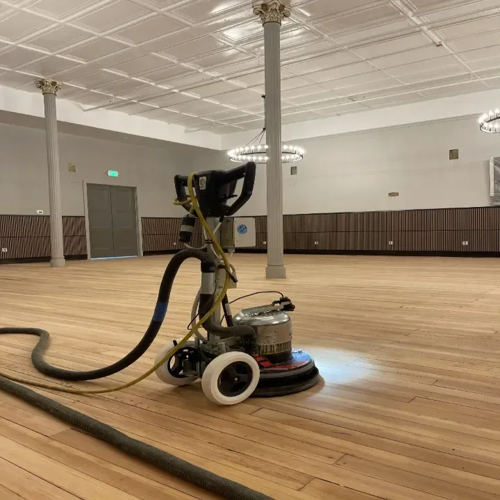 Floor sander on a hardwood floor in a spacious, empty event room. First sanding.