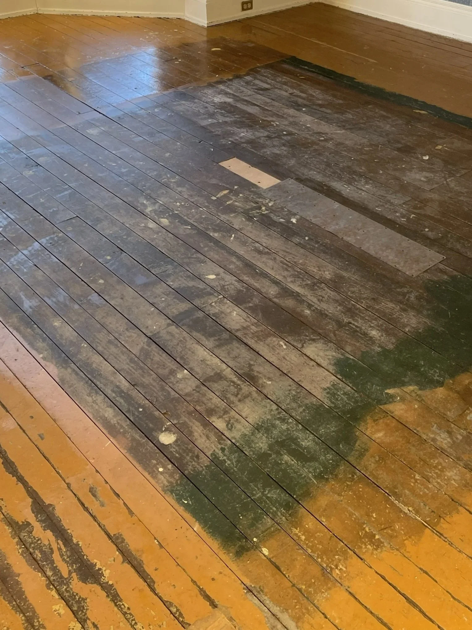 Partially refinished hardwood floor with old, scratched, and worn sections, some areas stripped and sanded down.