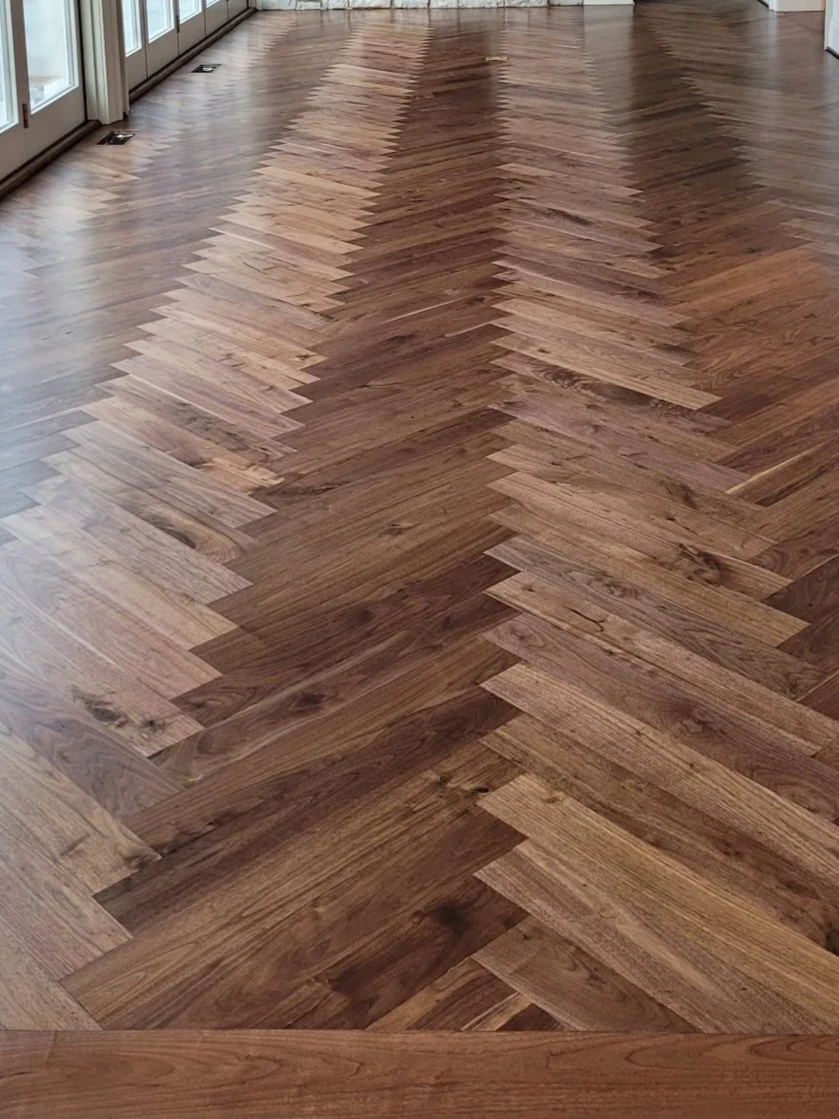 Wooden herringbone-patterned floor near a row of windows with sliding glass doors.
