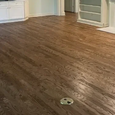 Empty hardwood floor room with a round vent cover near the center.