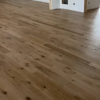 Interior of a house under construction, featuring unfinished white walls and natural wood floors.