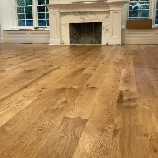 Empty living room with hardwood flooring, large windows, and a fireplace.