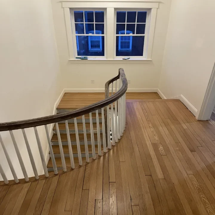 Empty staircase landing with hardwood floor and a curved wooden handrail.