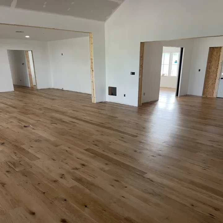 Interior of a house under construction, featuring unfinished white walls and natural wood floors.