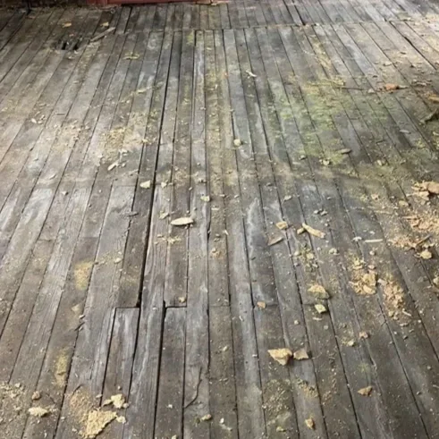 A before photo of a weathered wooden floor with scattered debris.