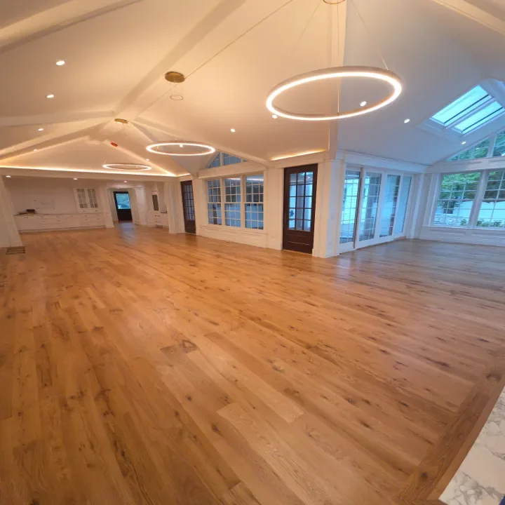 Spacious, empty room with hardwood floors, large windows, and modern circular ceiling lights.