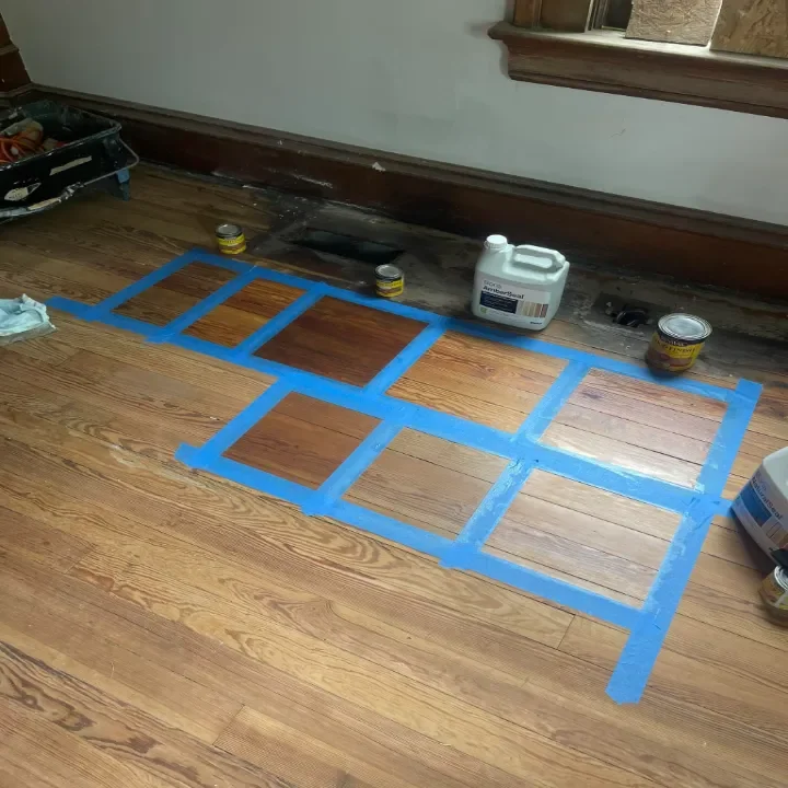 Wood floor with painter's tape creating a grid pattern to test stain choices.