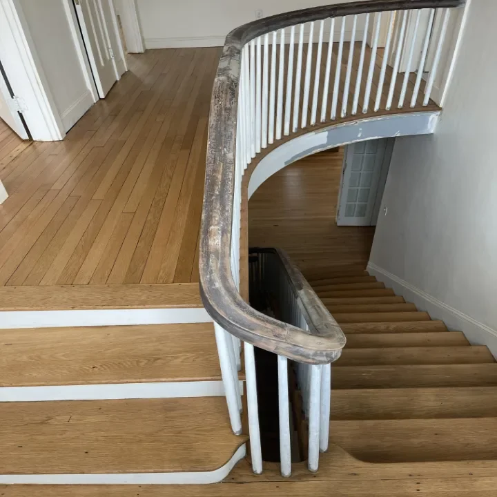 Top view of a wooden staircase with a curved handrail, showing the finished upper landing.