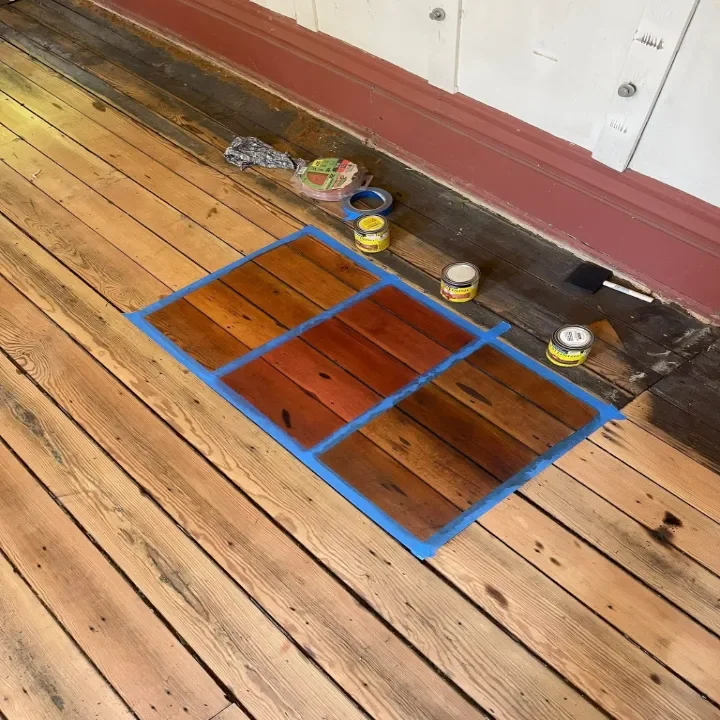 A wooden floor with a square outline taped off to test stain colors.