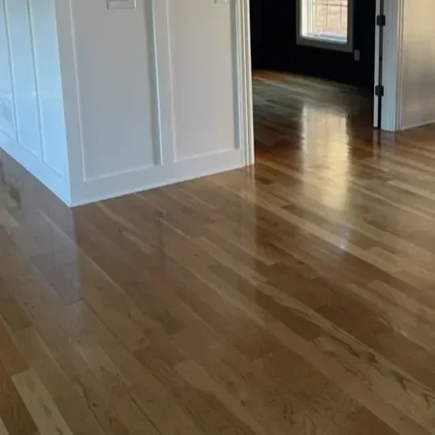 Interior view of a hardwood floor near a white wall and dark doorway with a window.