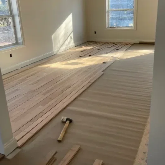 Room under renovation with wood flooring being installed, hammer and wood planks on the floor.