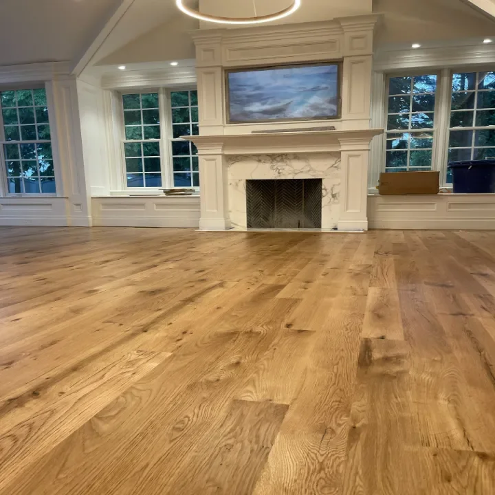 Empty living room with hardwood flooring, large windows, and a fireplace.