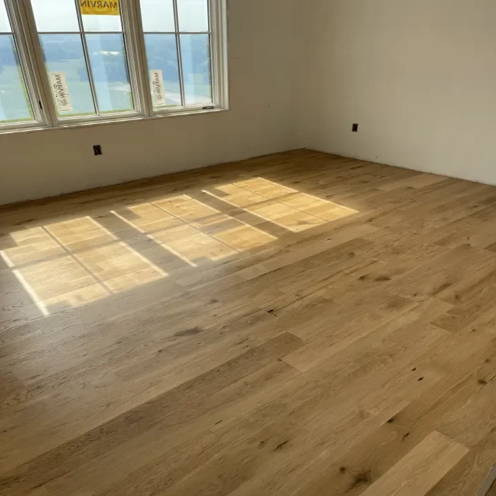 Empty room with hardwood floors and large windows letting in natural light.