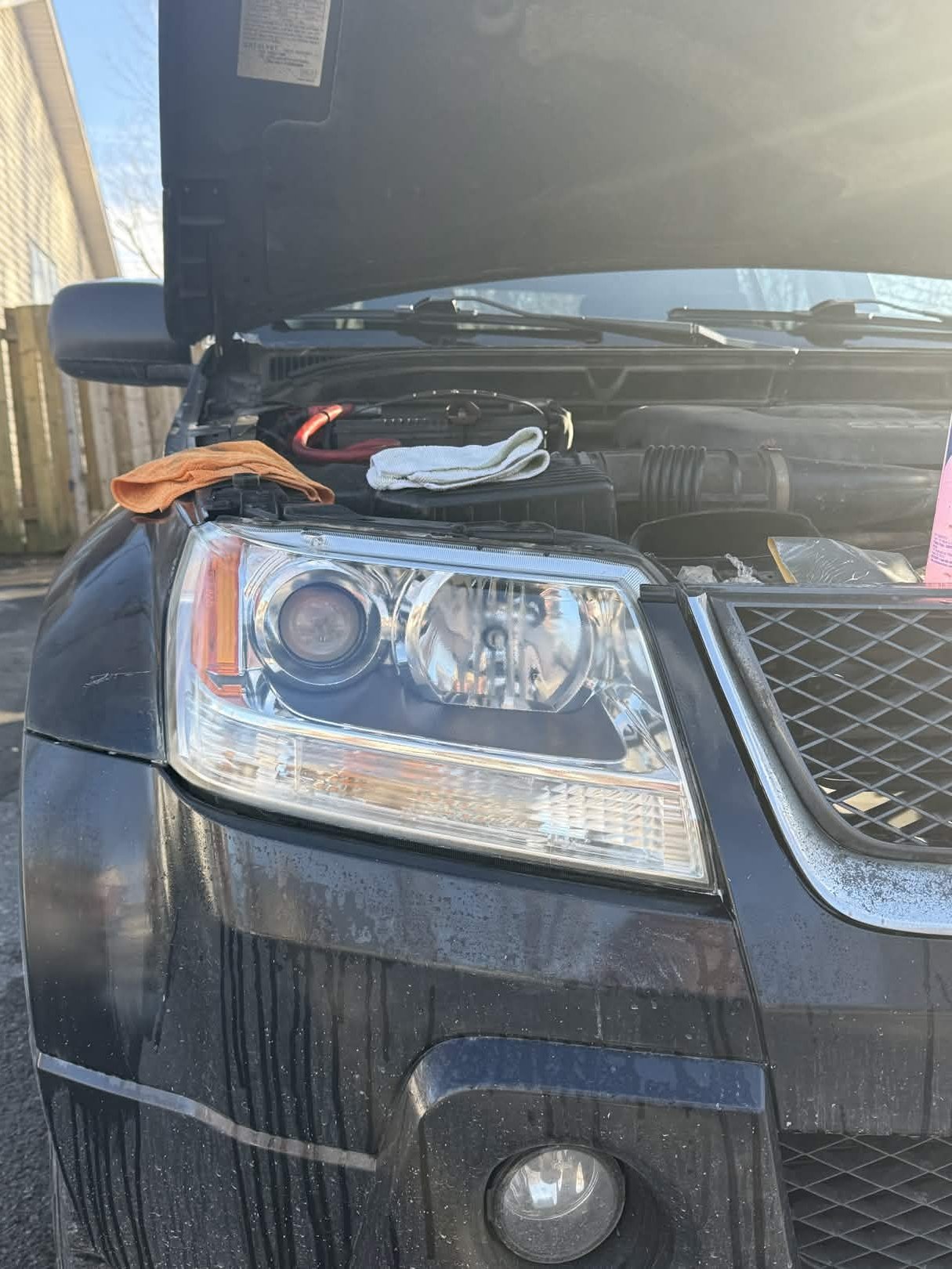 Close-up of the front of a black SUV with its hood open, showing the headlights and engine bay, with a cloth placed on the engine.