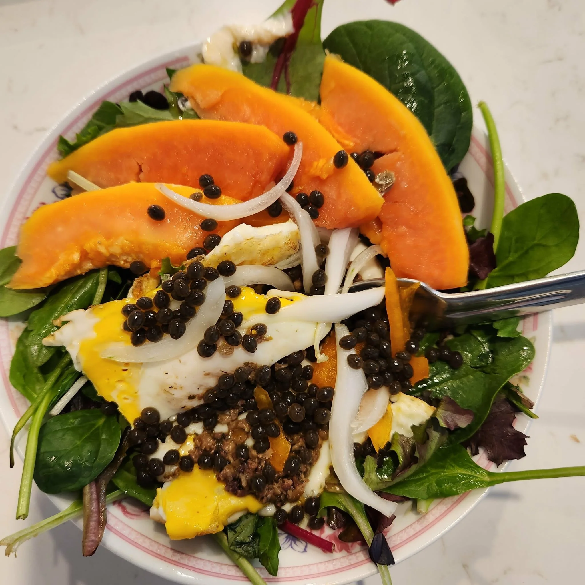 Mixed salad with greens, sliced roasted butternut squash, sliced onions, a poached egg, black peppercorns, and a fork.