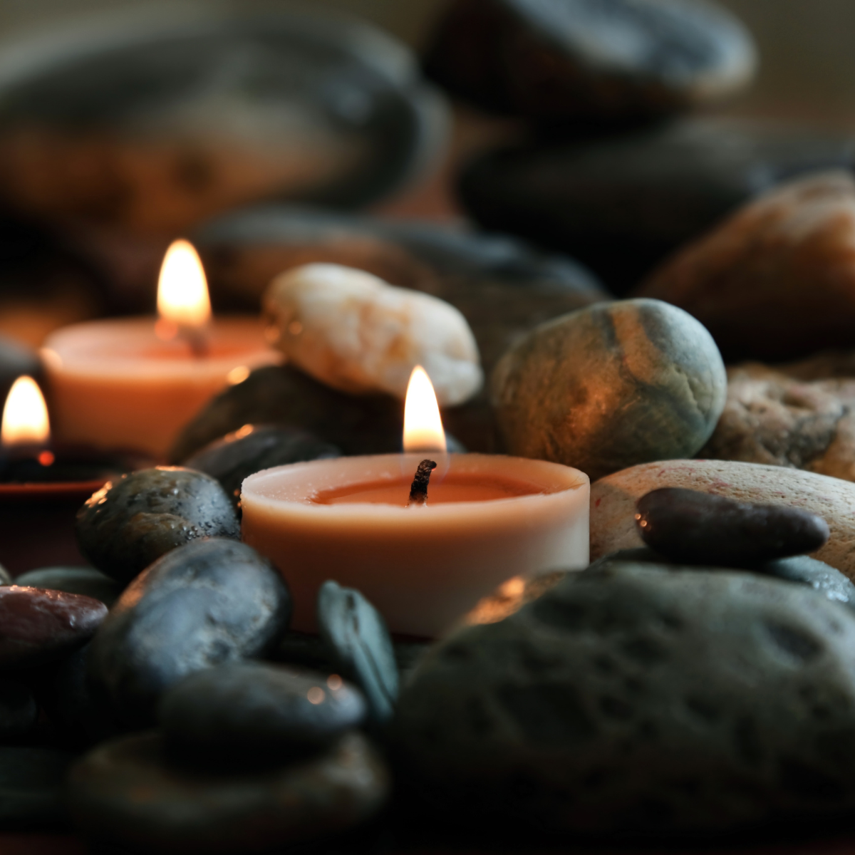Three candles surrounded by smooth stones, with flickering flames creating a calming scene.