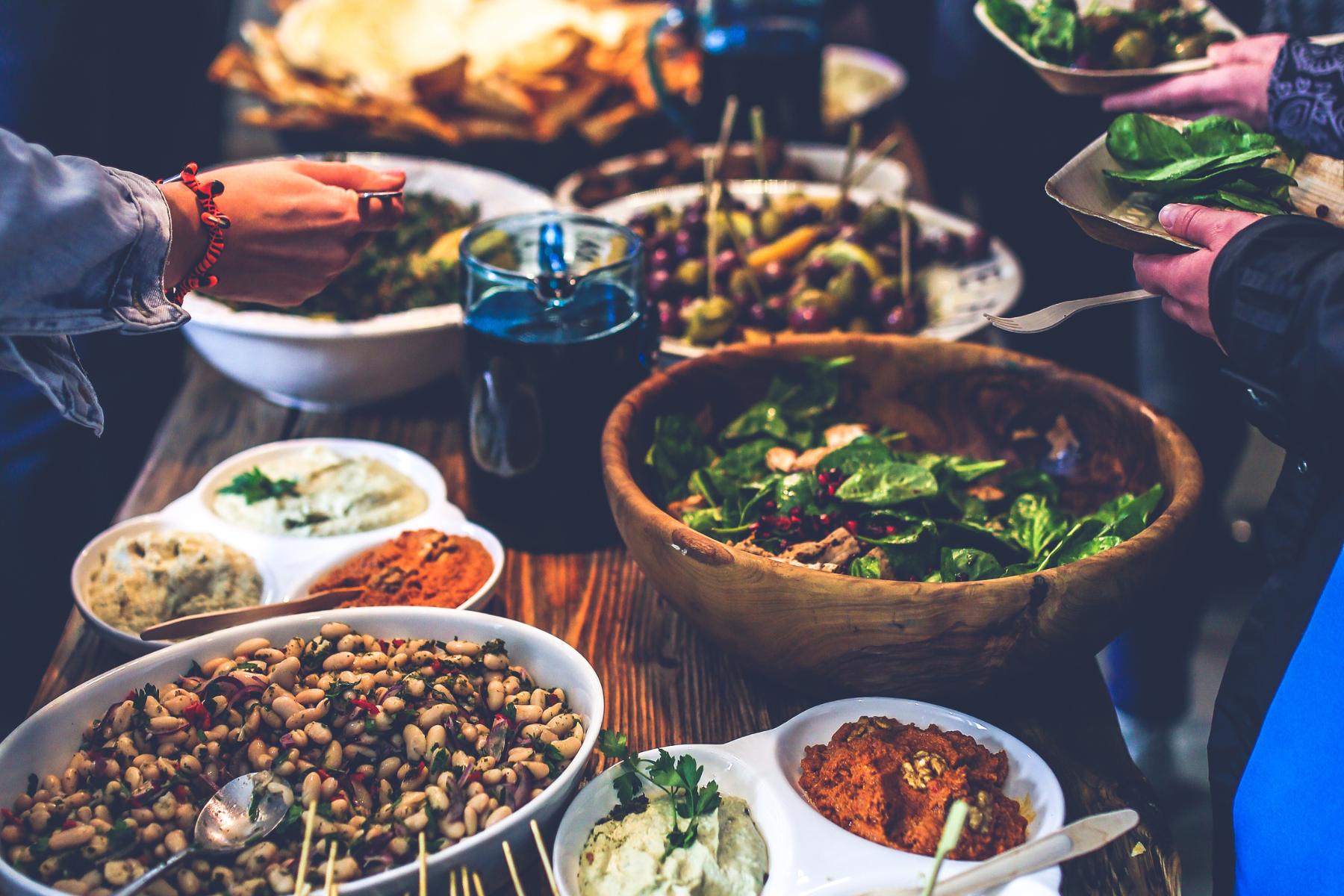 People serving themselves food from a buffet at a gathering and potluck of community and friends. With various salads, beans, and dips.