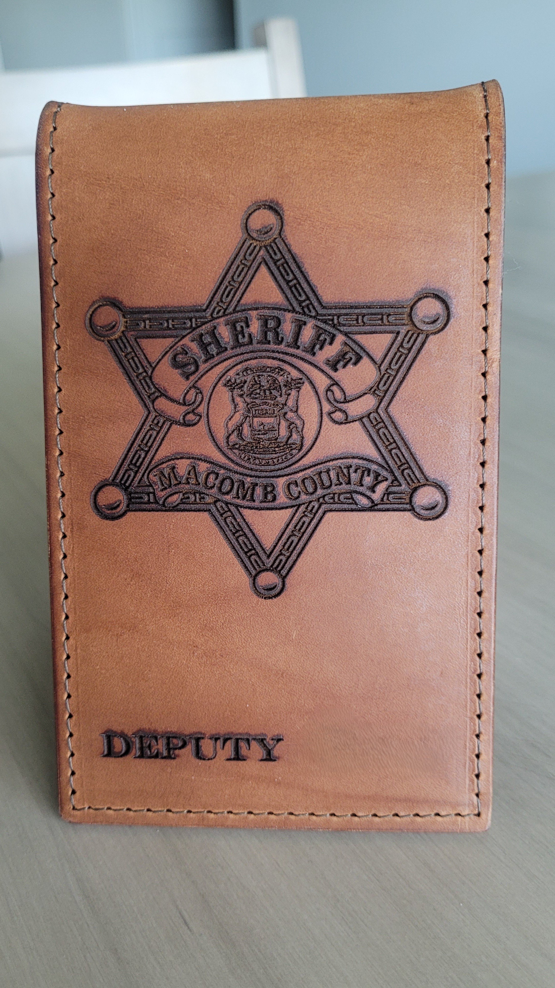 A tan leather badge holder with a sheriff's badge embossed on it, labeled 'Deputy' at the bottom.