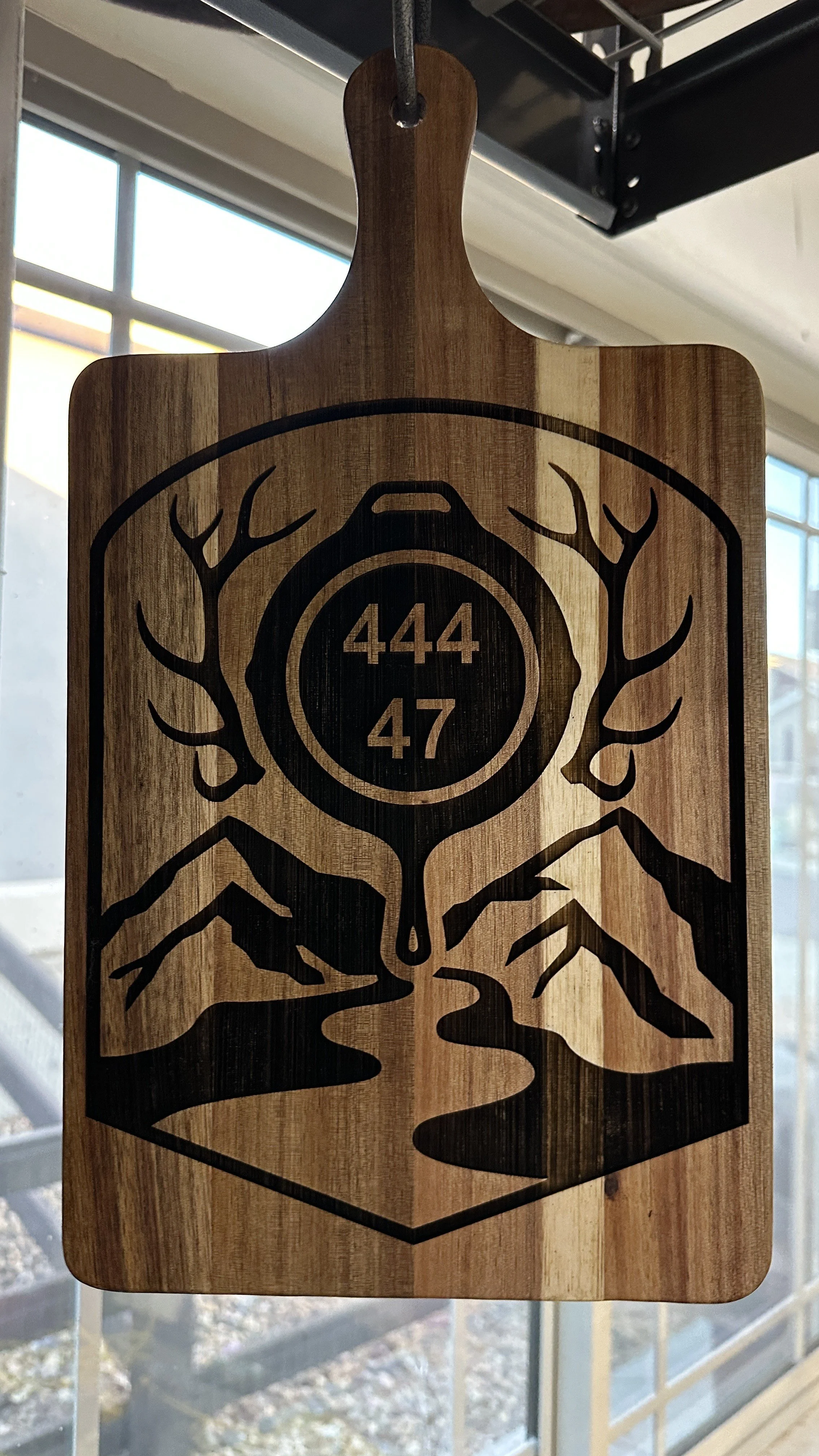 Wooden cutting board with engraved design of a deer and a circular emblem with the numbers 444 and 47.