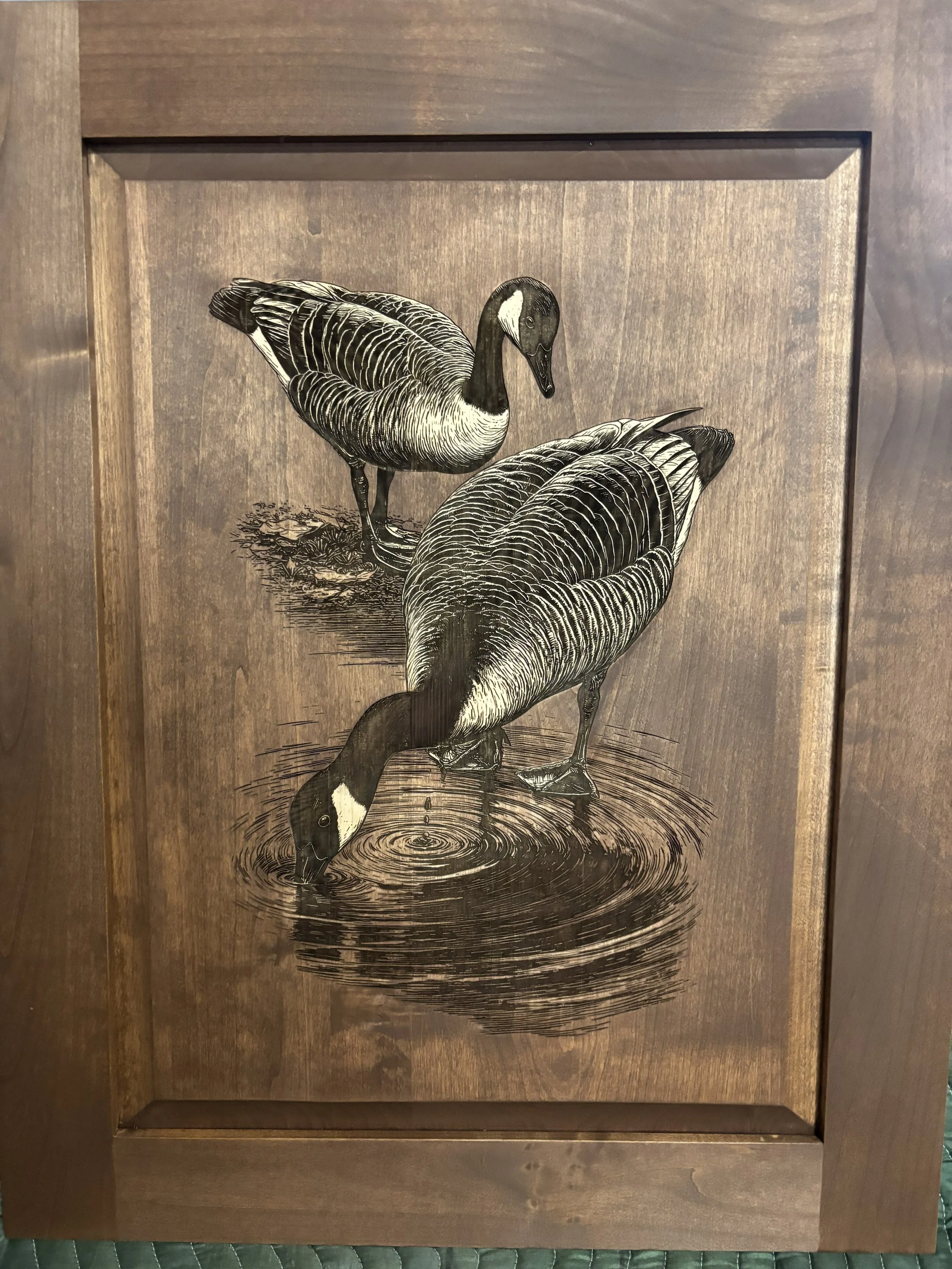 Black and white illustration of a goose standing on water next to its reflection, framed in wood.