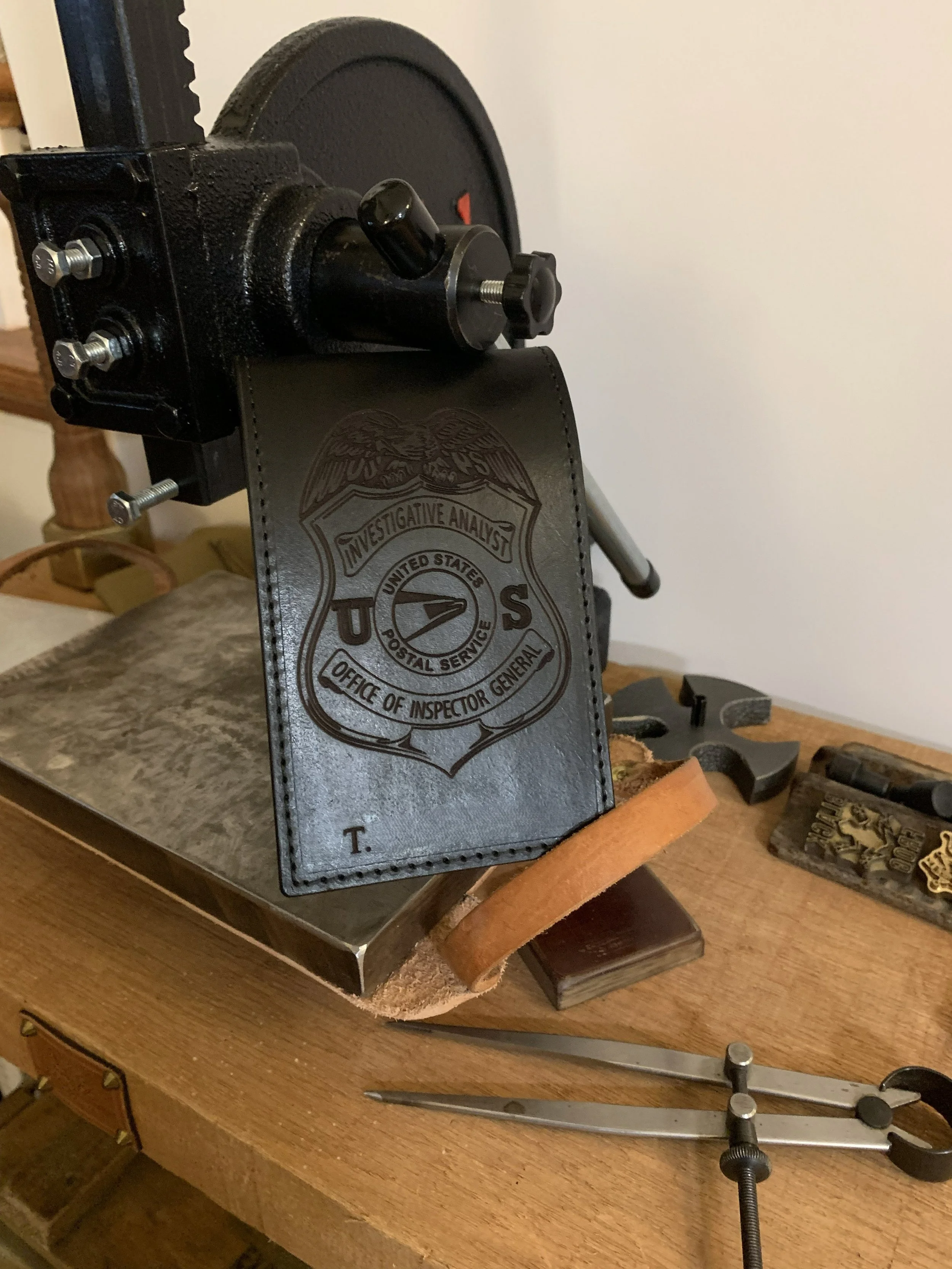Close-up of a USPS badge with the logo, attached to a metallic surface, on a wooden table surrounded by tools and small parts.