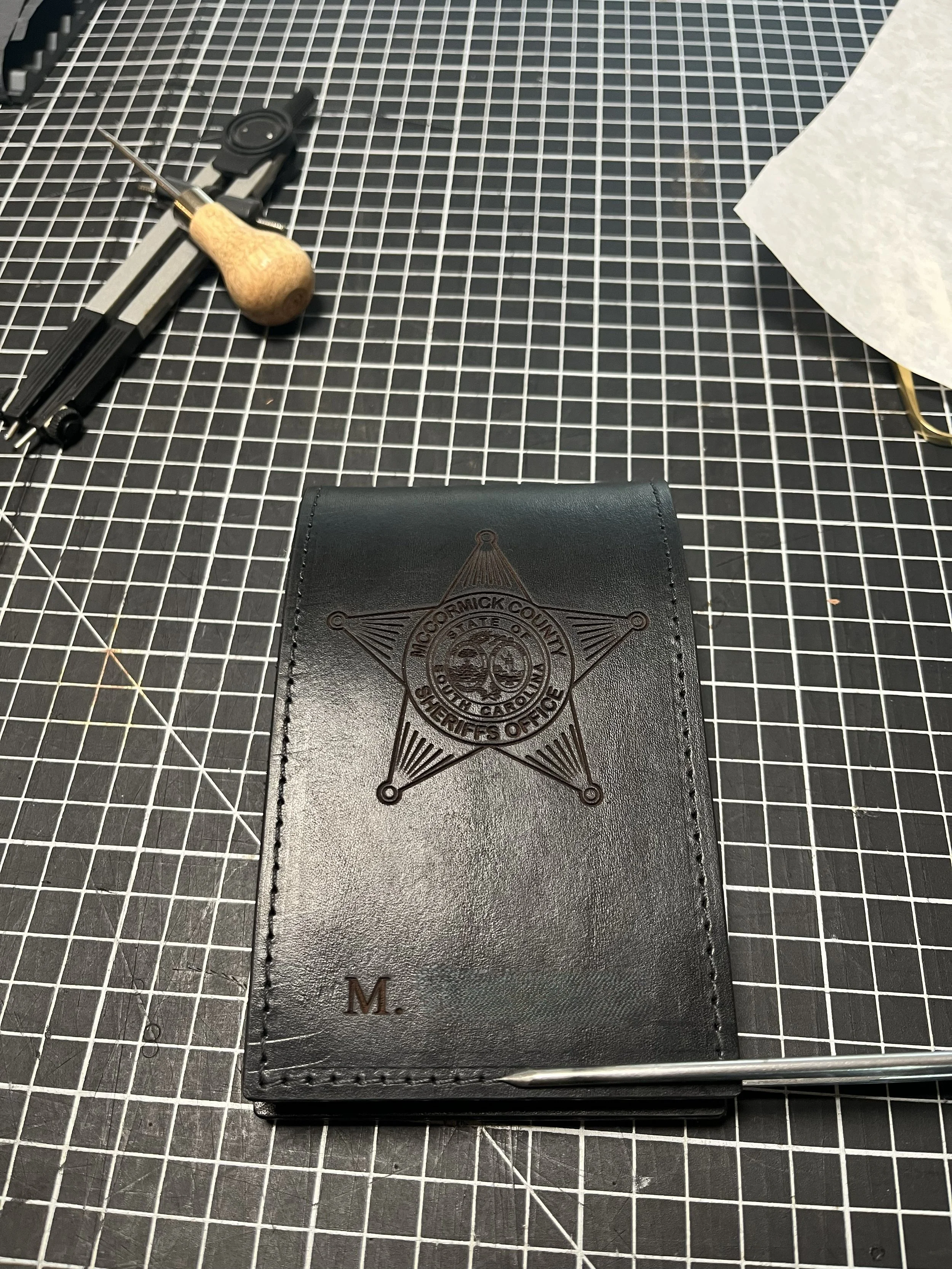 A pistol with a wooden handle and a metal barrel resting on a black cutting mat with a grid pattern.