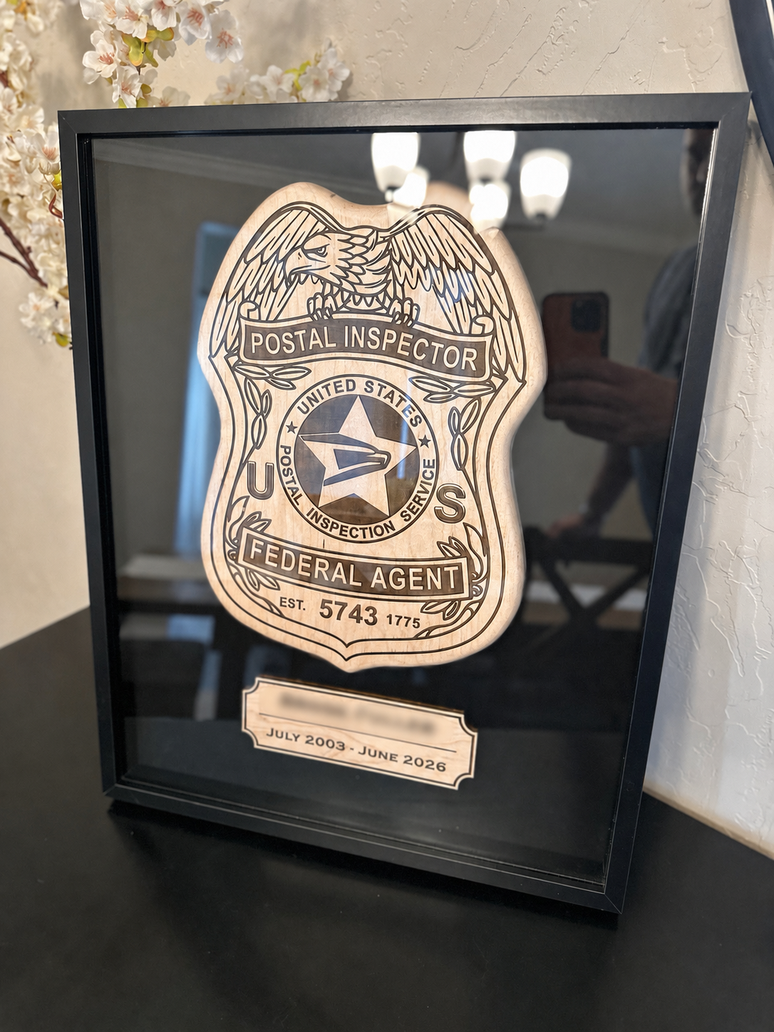 Decorative wooden wall plaque inside a glass frame with a Postal Inspector badge, including an eagle, star emblem, and text indicating a Federal Agent, with dates July 2003 to June 2026.